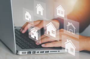 Hands typing on a laptop with floating icons of houses, representing online real estate or property listings. The image conveys a digital interface for browsing or managing real estate options through technology.